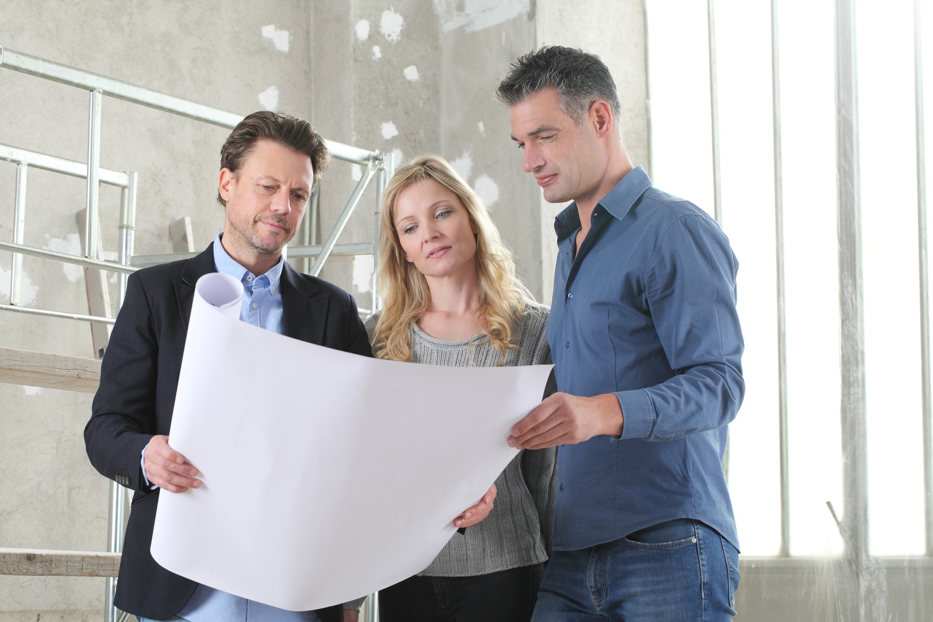 Architect showing house design plans to a young couple. House building goal concept. Meeting at interior construction site to talk about house appearance, interior decoration and home layout